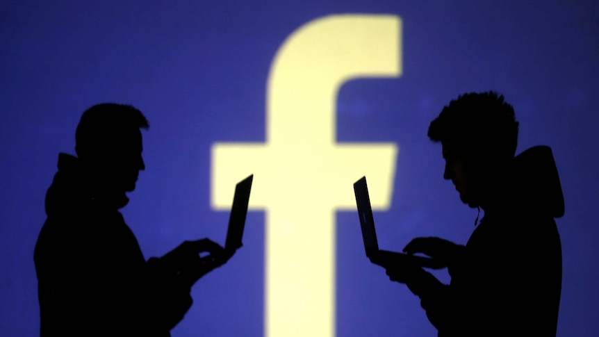 Силуэты двух людей за ноутбуками на фоне логотипа Facebook