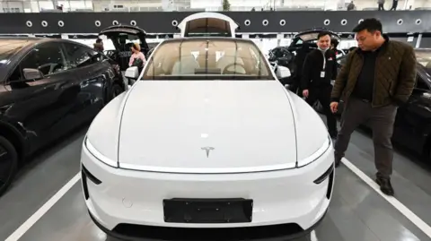Люди рассматривают белый автомобиль Tesla в шоуруме в Пекине