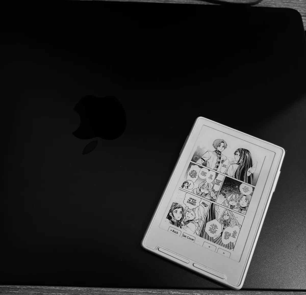 Страница манги, напечатанная на Xteink X3, лежит на закрытом MacBook